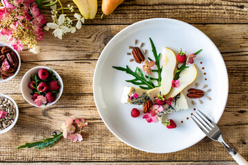 Fresh salad - blue cheese, raspberries, pear, arugula and pecan nuts on wooden background
