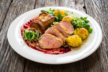 Fried pork loin with boiled potatoes and fresh vegetables on wooden table
