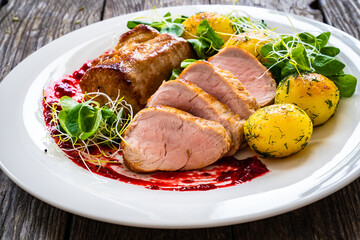 Fried pork loin with boiled potatoes and fresh vegetables on wooden table
