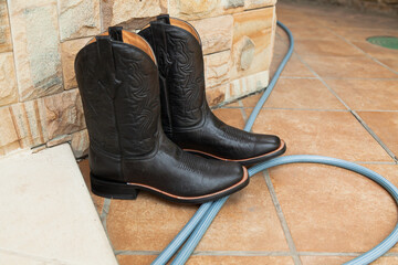 Cowboy boots and rubber hose stand on ceramic tile....