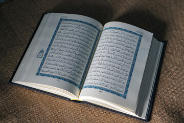 Fototapeta premium Kudus, Indonesia - August, 2022 : The Quran, also romanized Qur'an or Koran, is the central religious text of Islam, believed by Muslims to be a revelation from God (Allah). Brown sack background.