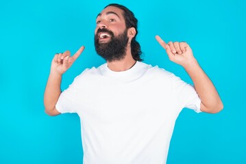 Fototapeta premium Cheerful young bearded man wearing white T-shirt over blue studio background demonstrating hairdo