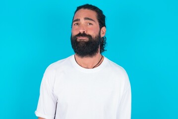 Fototapeta premium young bearded man wearing white T-shirt over blue studio background depressed and worry for distress, crying angry and afraid. Sad expression.