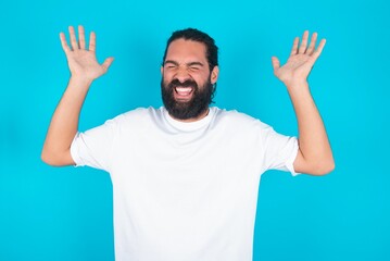 young bearded man wearing white T-shirt over blue studio background goes crazy as head goes around feels stressed because of horrible situation