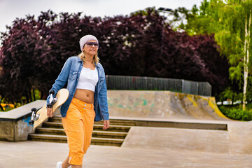 Young woman walking with skateboard in skate park