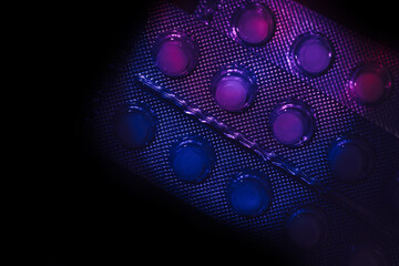 Pills or drugs in a package under neon light on a dark background pattern for design..