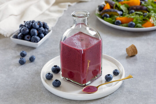 Salad dressing or Blueberry sauce with fresh blueberries, oil, balsamic vinegar, honey, salt and pepper served in glass bottle. Ingredients and plate with salad on background. Horizontal.  