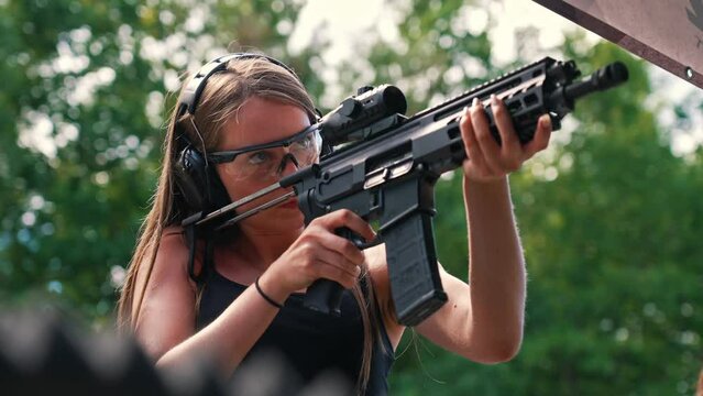 Young caucasian woman wearing protective goggles and headphones practising with submachine gun on outdoor shooting range. Horizontal shot. High quality 4k footage