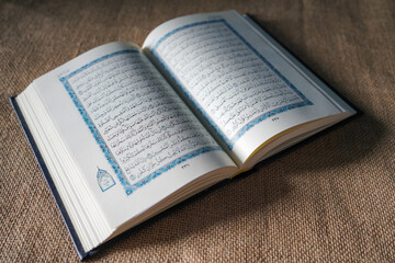 Kudus, Indonesia - August, 2022 : The Quran, also romanized Qur'an or Koran, is the central religious text of Islam, believed by Muslims to be a revelation from God (Allah). Brown sack background.