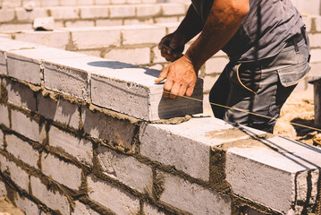 Professional construction worker laying bricks and mortar - building external house walls. Construction site detail -closeup of hand adjusting bricks