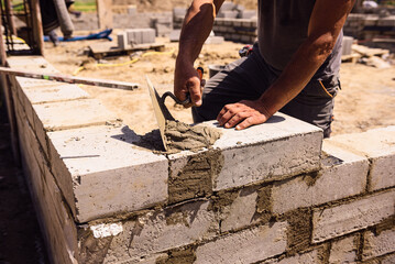 Professional construction worker laying bricks and mortar - building external house walls. Construction site detail -closeup of hand adjusting bricks