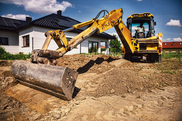 Fototapeta Excavator working at house construction site - digging foundations for modern house. Beginning of house building. Earth moving and foundation preparation. obraz