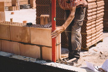 Professional construction worker adjusting bricks and mortar - building external house walls. Construction site detail - closeup of hand adjusting bricks