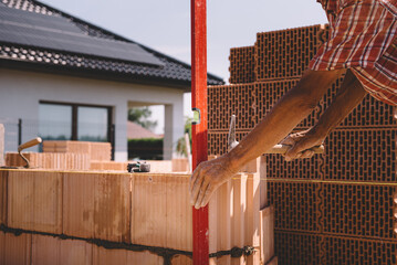 Professional construction worker adjusting bricks and mortar - building external house walls. Construction site detail - closeup of hand adjusting bricks