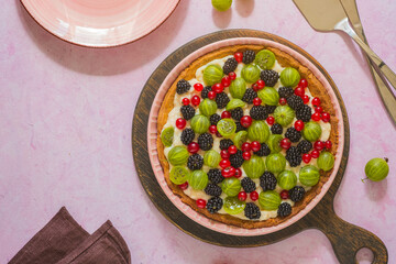 Dessert, shortbread tart with assorted berries and custard in a pink ceramic form on a pink concrete background. Dessert recipes with berries.