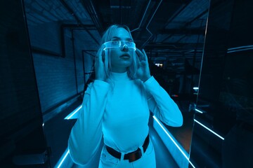 A blonde in neon glasses who is in a room with blue light.