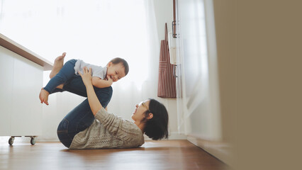 Happy Asian Mother lifting her little son in the air on the floor. Loving family having fun games...