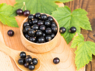 Fresh blackcurrant berries in a bowl on a wooden table near green leaves. Juicy natural currant fruits. Black currant
