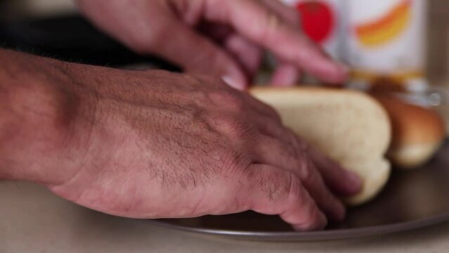 A man's hand opening a hot dog bun.