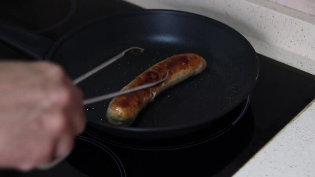 Man grilling a bratwurst (German white sausage) in a pan. German food concept.