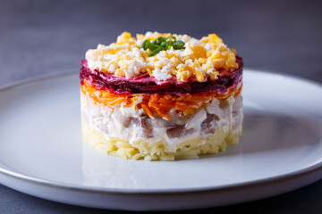 Herring salad under a fur coat. Traditional Russian multilayered salad from herring, beets, potatoes, carrots and eggs. Close-up, grey background.