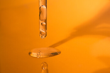 Close-up glass dropper with a transparent liquid cosmetic texture on a bright orange background...