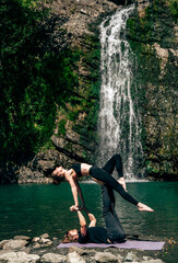 Acro yoga. Young man holds his girlfriend in forest near  waterfall. Active lifestyle concept.