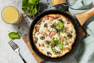 Italian breakfast dish. Rustic omelette (frittata) with mushrooms and bacon on a cast iron pan. View from above.