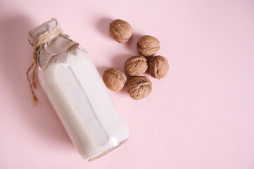 Flat lay Bottle with wholesome plant based milk and walnuts on pink background with copy space. Healthy food and drink