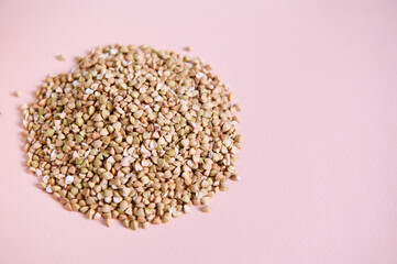 Selective focus. Heap of wholesome organic green buckwheat grains on pink background. Copy ad space. Vegan healthy food