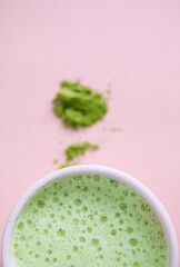 Partial view of a white cup of whipped green tea with foam and blurred powdered japanese matcha, over pink background
