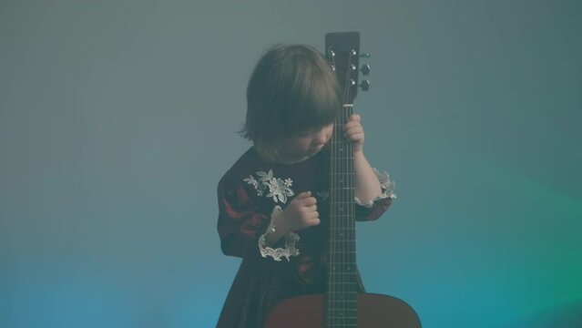 Cute little girl stands on stage in vintage dress and plays an acoustic guitar like a counter bass or cello. The concept of performing the author jazz and blues music. Hobbies and art among children