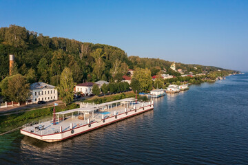 Fototapeta na wymiar Embankment of town on banks of Volga with buildings on hillside hidden in dense foliage Plyos Russia