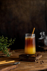Bumble coffee on a dark background. Espresso, orange juice, syrup in layers in glass with ice. Refreshing coffee drink. Coffee house menu, recipe. Copy space.