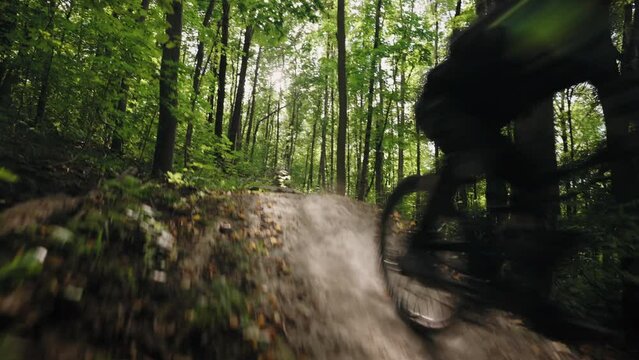 A cinematic shot of a professional cyclist on a mountain bike riding at high speed at the camera and jumping over forest obstacles and trampolines. Atmospheric shots of driving through the forest