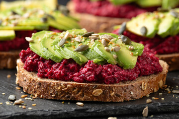 Avocado, beetroot hummus toast on dark sourdough bread topped with pumpkin, sunflower, hemp and flaxseed. Vegan, vegetarian super food