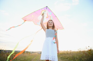 happy child girl with a kite running on meadow in summer in nature