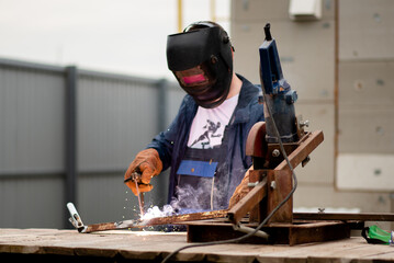 The man works with a welding machine. He is wearing a welder's protective mask and protective gloves. A rare working profession.