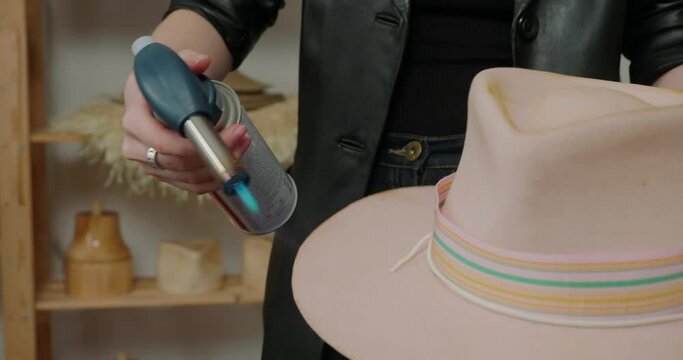 Milliner burns brim of finished felt hat with equipment