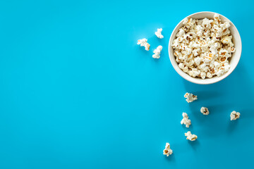 Plate with popcorn on a blue background, flat lay.