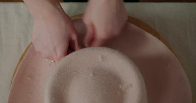Hands of milliner add wind cord around felt hat at table