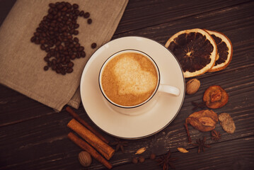 A mug of coffee on a wooden background with spices.