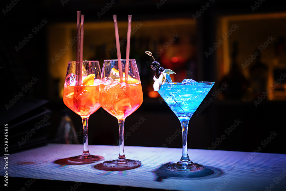 Wall mural Three glasses with fresh alcohol drinks and with ice cubes on the bar counter of a night club - lifestyle concept