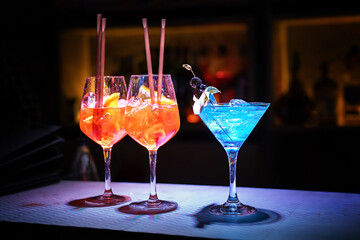 Three glasses with fresh alcohol drinks and with ice cubes on the bar counter of a night club -...