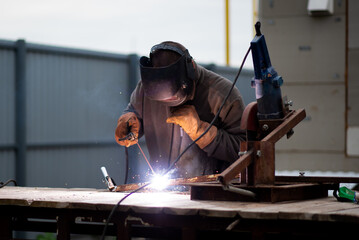The man works with a welding machine. He is wearing a welder's protective mask and protective...