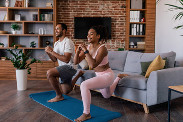 Happy young african american family in sportswear doing leg exercises, stretching or practicing yoga