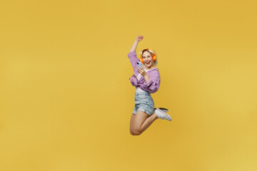 Obraz premium Full body side view young blonde woman 20s in nk tied shirt white t-shirt jump high hold use mobile cell phone do winner gesture isolated on plain yellow background studio People lifestyle concept