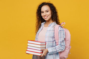 Side view young smiling happy fun black teen girl student she wearing casual clothes backpack bag hold pile of book isolated on plain yellow color background. High school university college concept.