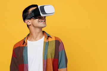 Young happy gambling middle eastern man 20s he wear casual shirt white t-shirt watching in vr headset pc gadget play games isolated on plain yellow background studio portrait People lifestyle concept.