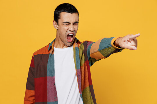 Young Angry Sad Mad Furious Middle Eastern Man 20s He Wearing Casual Shirt White T-shirt Point Index Finger Aside Scream Isolated On Plain Yellow Background Studio Portrait People Lifestyle Concept.